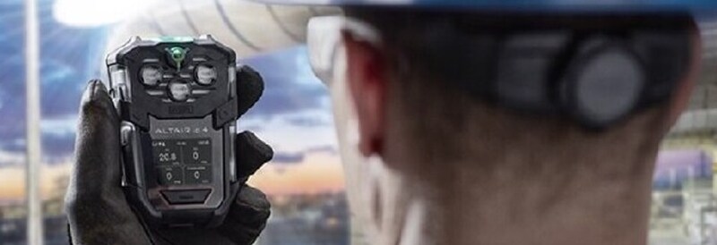 A man wearing a hardhat uses a gas detection instrument.