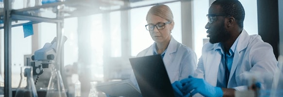 A woman and man discuss what they see on their computers in a chemistry lab.