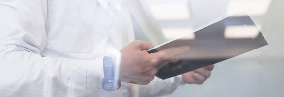 A man in a lab coat holds a notebook.
